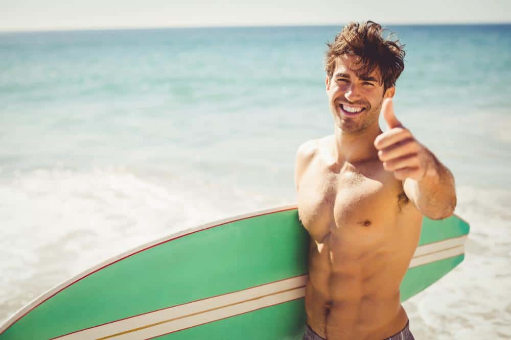 man with surfboard giving thumbs-up