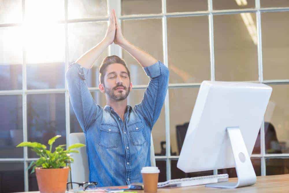 Image of a man lifting his arms over his head at a work desk.