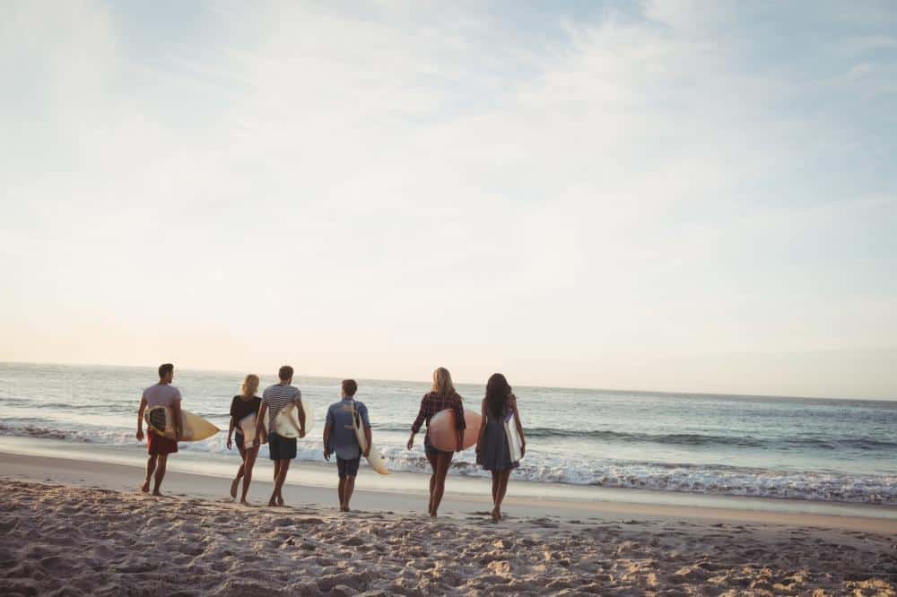 images of friends in recovery with surfboards walking toward the beach