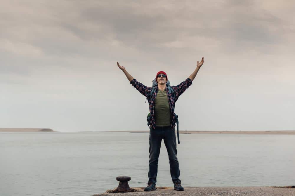 man on pier opening his armes to the sky with face raised