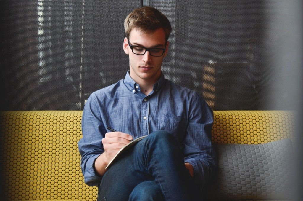 man in denim jacket sitting and writing affirmations